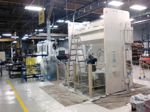 Man with a respirator mask paint spraying a large industrial machine in a manufacturing environment.