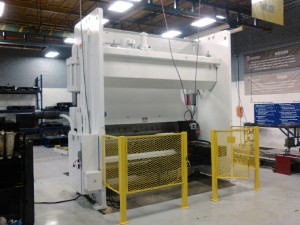 Large white industial machine with a yellow metal safety gate in front of it in a manufacturing environment.